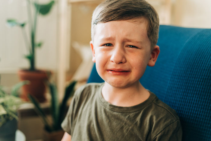 Young boy crying with tears on his face, sitting indoors, illustrating emotional impact of telling SIL&rsquo;s kids their dad passed away.