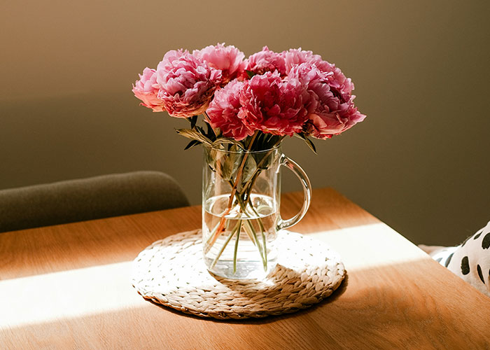 Glass vase with pink flowers on a wooden table symbolizing emotions in a man asking how to make her feel what he feels.