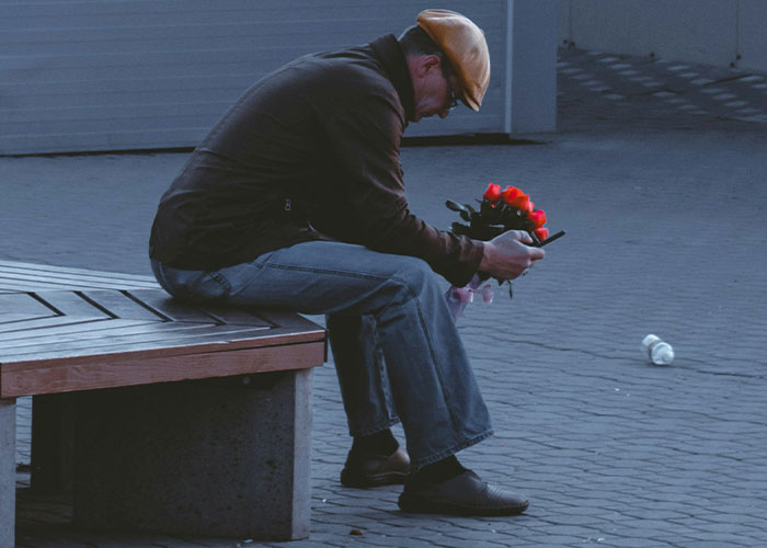 Man sitting alone on bench holding red roses, reflecting on feelings after date leaves wife crying and reality check.