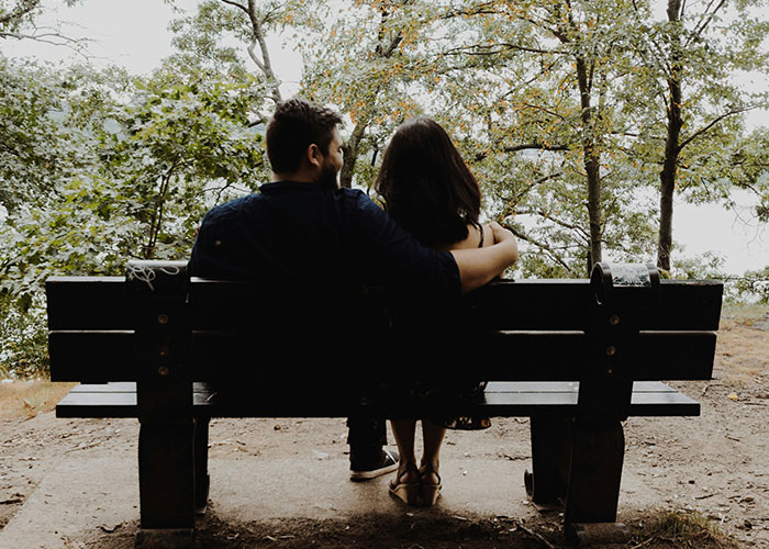 Couple sitting on a park bench with the man embracing the woman, illustrating feelings and emotional connection after a date.