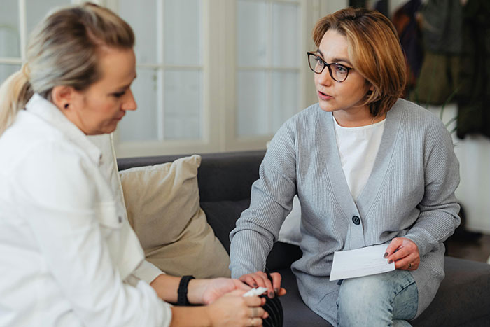Two women in a serious conversation indoors, reflecting on a flirty dad dropping off sweets at school. Two women in a serious conversation indoors, reflecting on a flirty dad dropping off sweets at school.