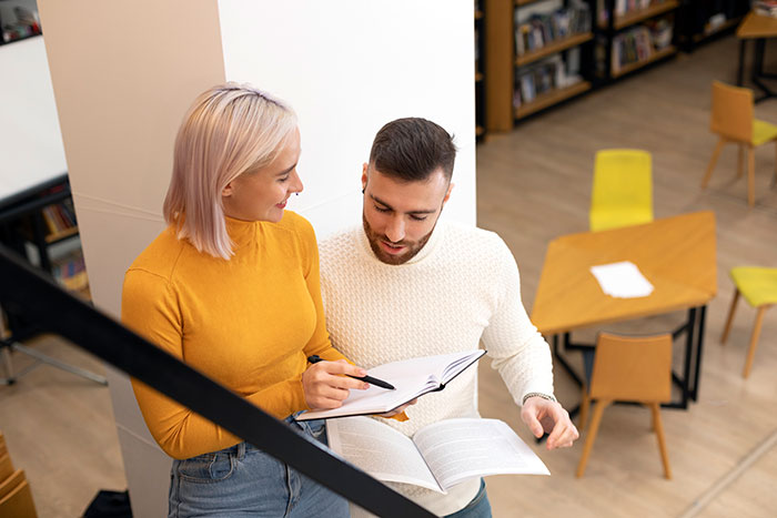 Man and woman discussing notes together in a school setting with flirty dad dropping off sweets nearby Man and woman discussing notes together in a school setting with flirty dad dropping off sweets nearby