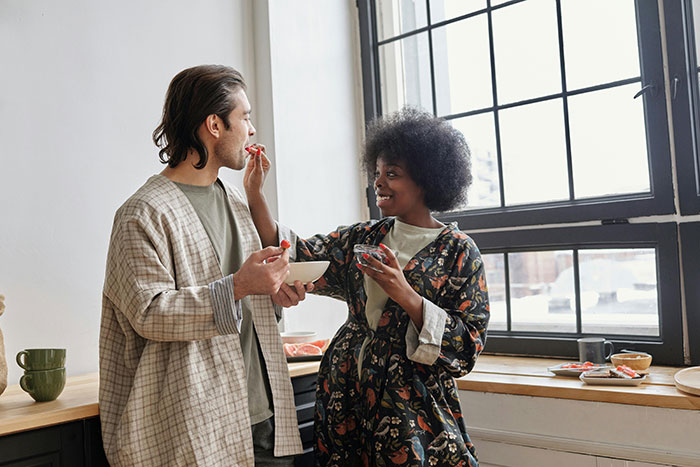 Woman supports husband during cross-country move, sharing a moment in cozy kitchen with natural light from large windows.