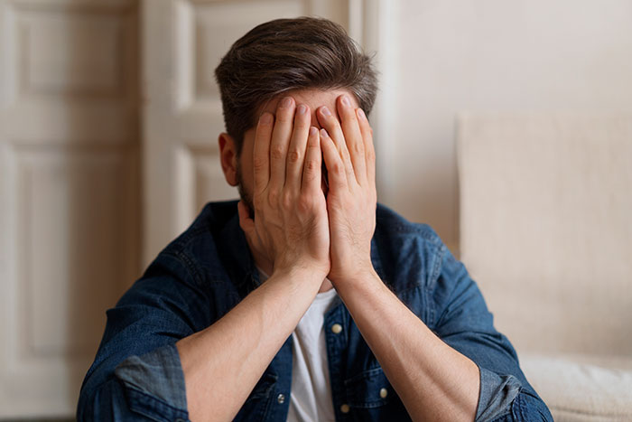 Man covering his face with hands, showing jealousy and regret, reflecting emotions at a wedding event.