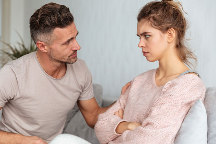 Man undermining wife's job, arguing and defensive while she looks upset and refuses to laugh along.