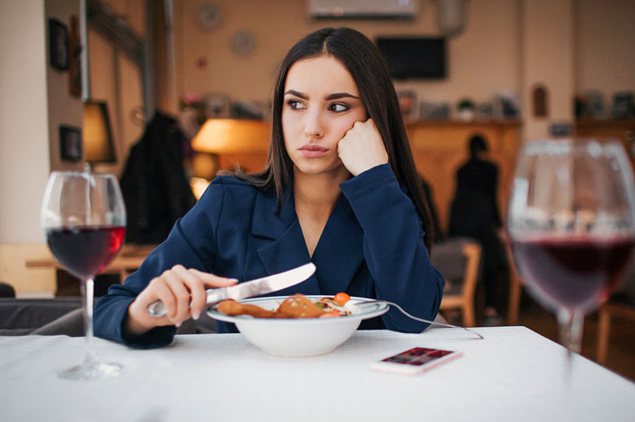 Woman looking upset at restaurant, reflecting tension related to man undermining wife&rsquo;s job and defensiveness.