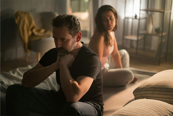 Man and woman sitting apart on bed looking upset, illustrating woman's husband leaves her after being hit on.