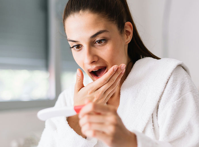 Woman surprised with pregnancy test, showing shocked reaction while holding the test in a bright, cozy room. Woman surprised with pregnancy test, showing shocked reaction while holding the test in a bright, cozy room.