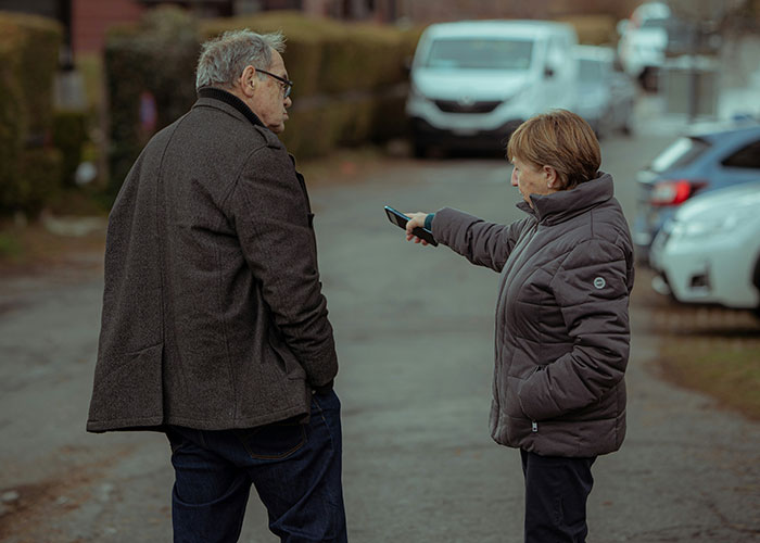 Older man and woman having a serious conversation outdoors, illustrating woman left to care for kids in flight after husband refuses