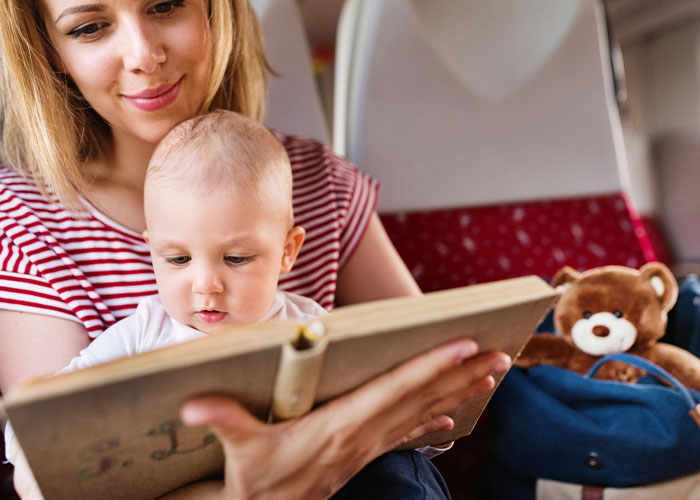 Woman caring for kids on flight, reading book to baby while husband refuses to help during travel journey.