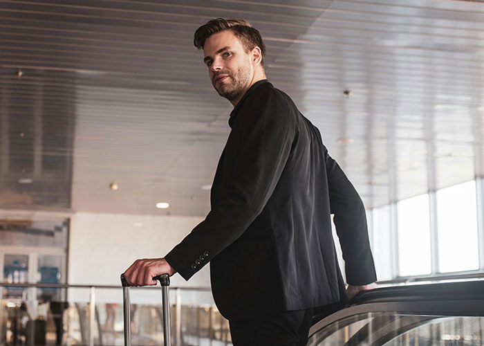 Man in black suit at airport with suitcase, representing husband refusing to care for kids during flight.