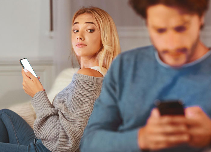 Wife looking insecure while her husband uses a phone, illustrating concerns about hubby connecting with mutual friend. Wife looking insecure while her husband uses a phone, illustrating concerns about hubby connecting with mutual friend.
