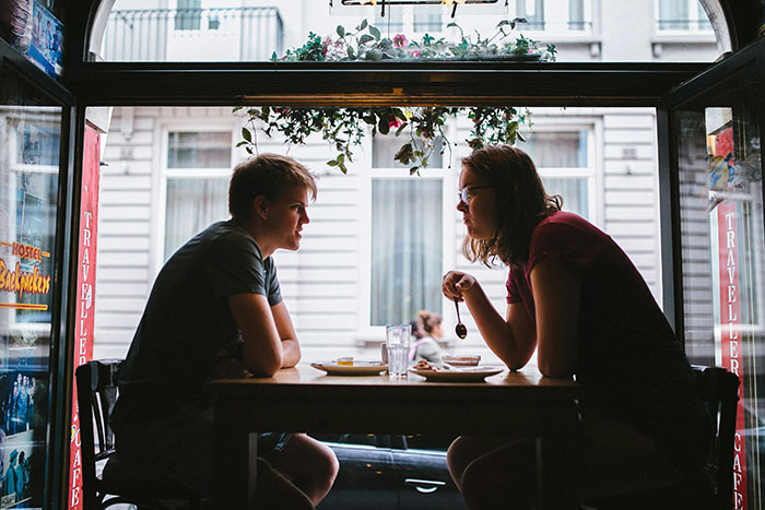 Woman seeking advice on talking sense into husband during serious conversation at caf&eacute; table, natural light from window.