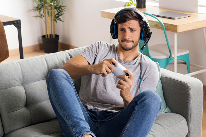 Young man wearing headphones playing video games on a controller, facing the end of his gaming days.