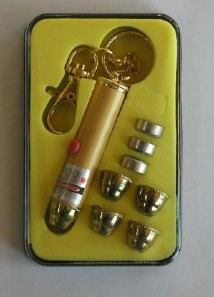 Gold cringey nineties fashion accessory kit with laser pointer, clips, and metallic caps in a yellow case.
