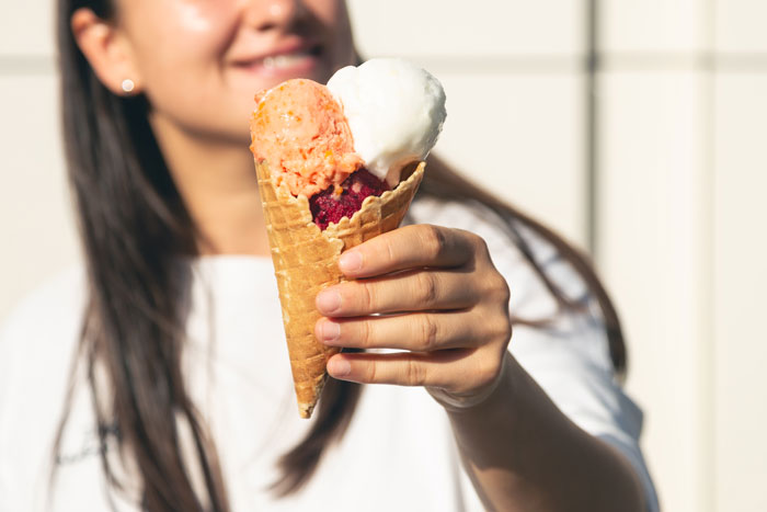 Woman holding ice cream cone with three scoops, illustrating mom tells SIL eating ice cream every night complicates parenting. Woman holding ice cream cone with three scoops, illustrating mom tells SIL eating ice cream every night complicates parenting.