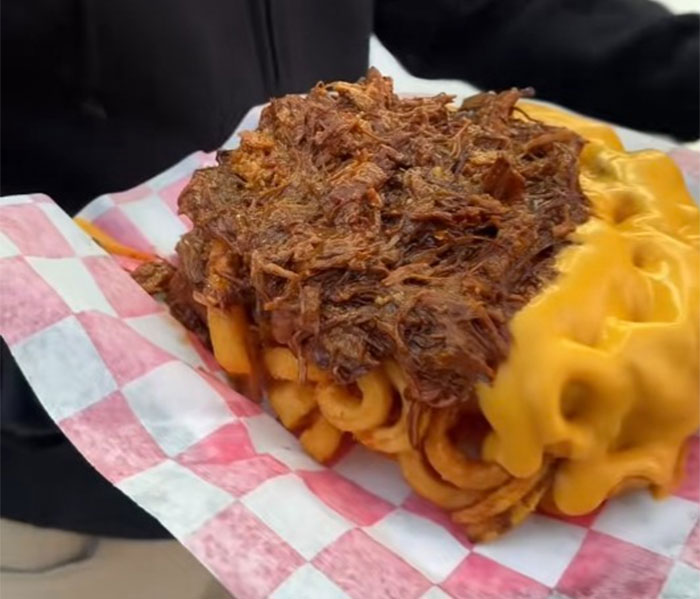 Curly fries loaded with pulled meat and melted cheese served at a county fair food stand.