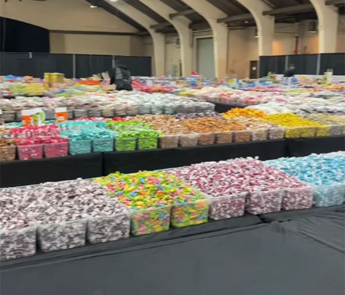 Various colorful county fair foods and candies displayed in clear bins inside a large indoor venue.