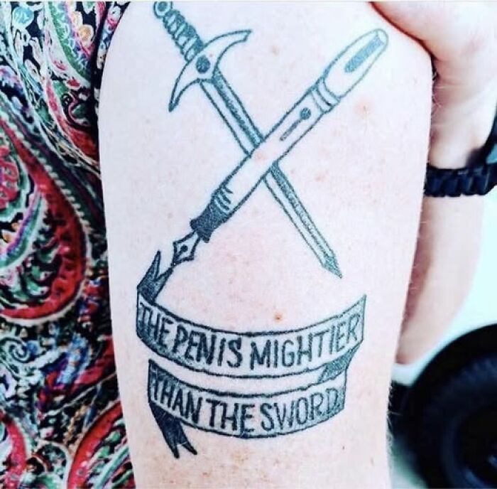Tattoo with a sword and a pen crossed, mistakenly inked with humorous text showing a permanent tattoo mistake.