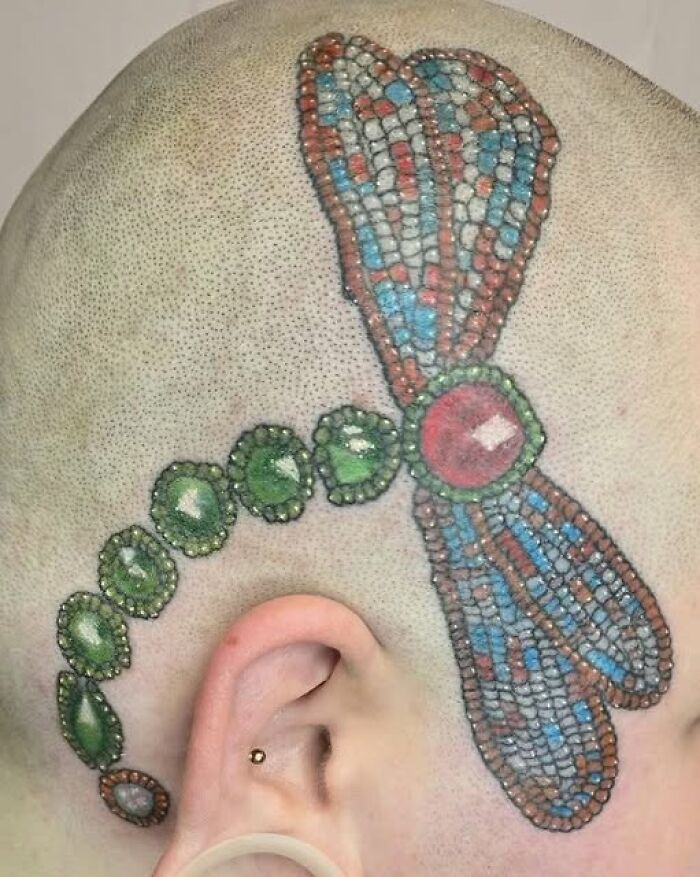 Colorful dragonfly tattoo with gemstone details on a shaved head, an example of people getting inked to look cool.
