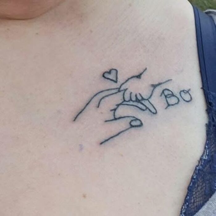 Tattoo of an adult hand holding a baby's hand with a small heart and the word Bo in black ink on chest.