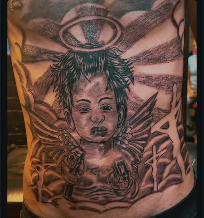 Tattoo of a baby angel with wings and guns, showcasing a permanent mistake in an ink design on a person's stomach.