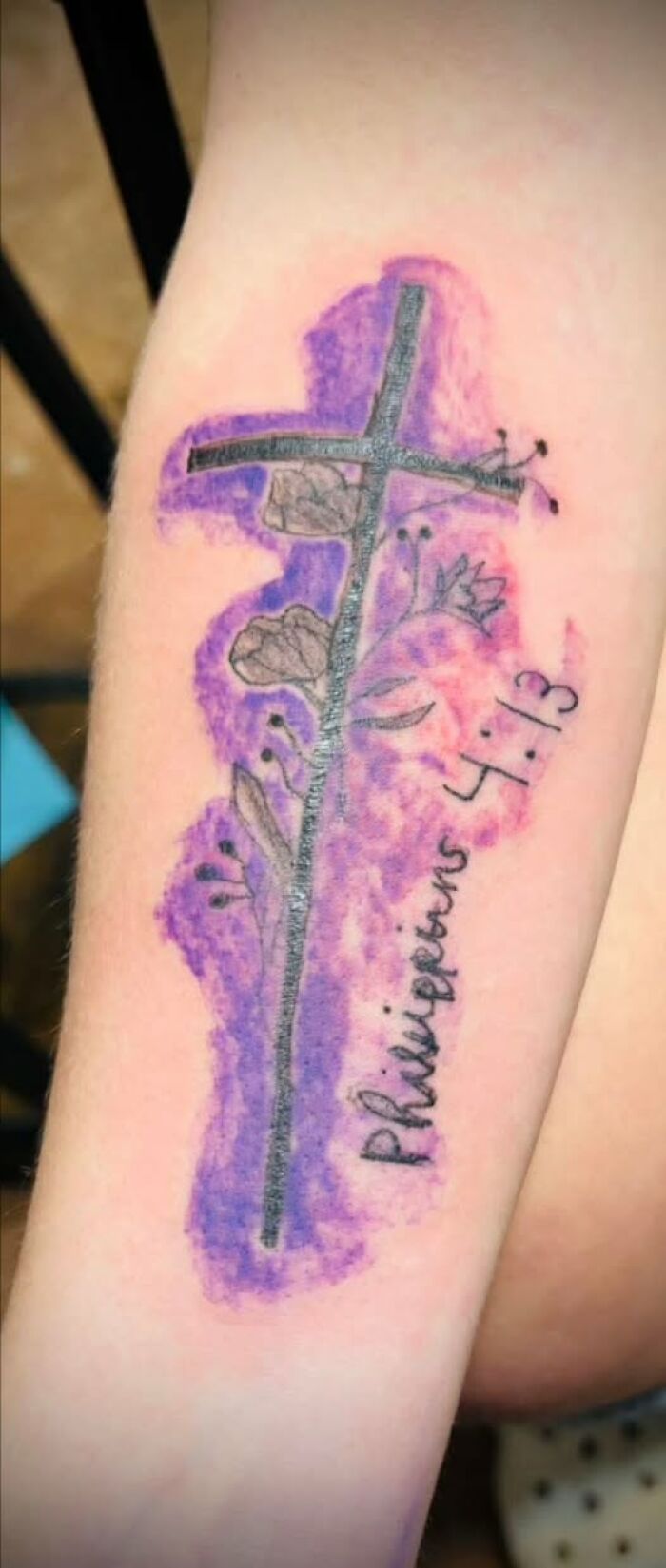 Tattoo with a cross and flowers featuring a misspelled Bible verse, showcasing a permanent mistake in inked design.