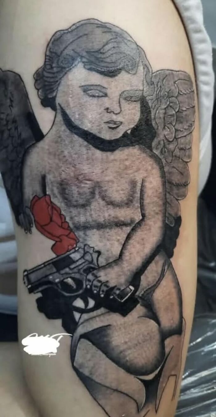 Tattoo of a cherub holding a gun with a red rose, an example of people getting inked to look cool but with a permanent mistake.