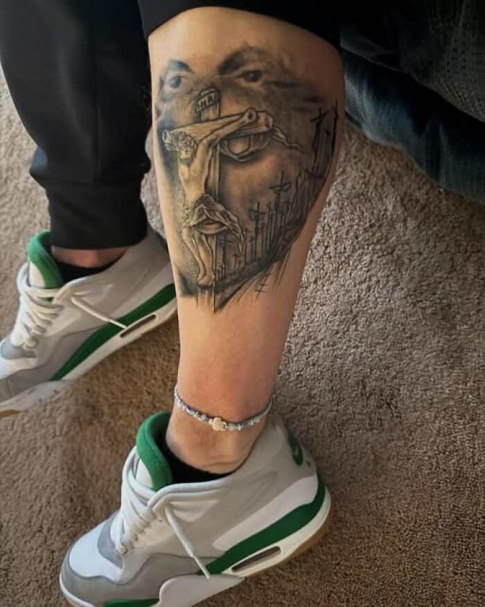 Leg tattoo depicting a religious crucifix scene with multiple crosses and a shaded face, showing inked permanent mistakes.