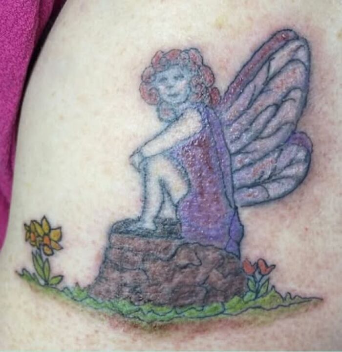 Tattoo of a fairy with wings sitting on a rock surrounded by flowers, an example of people getting inked with mistakes.