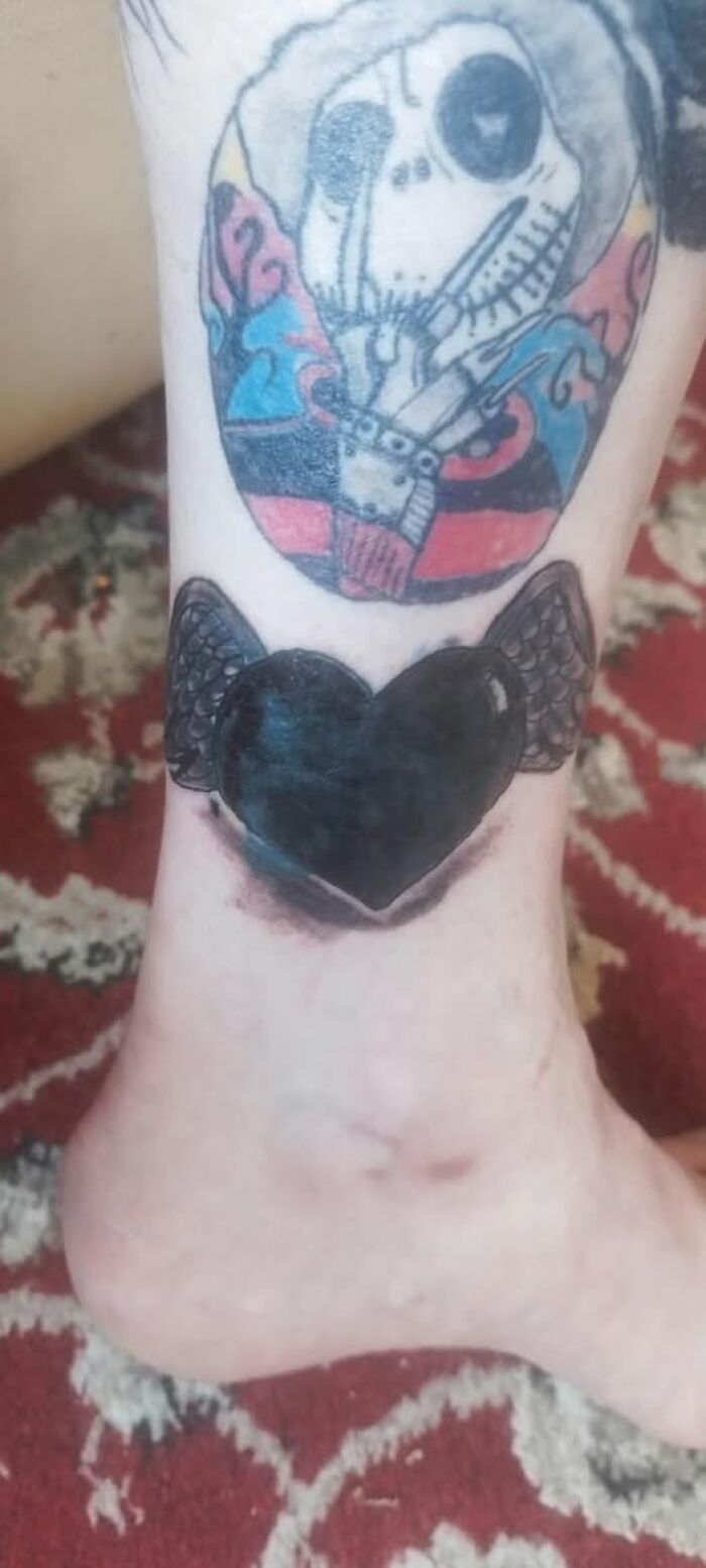 Close-up of an ankle with black heart and colorful skeleton tattoos showing inked mistakes on skin.
