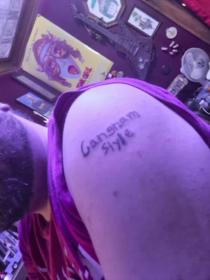 Tattoo fail showing a misspelled Gangnam Style ink on a person's upper arm in a colorful room.