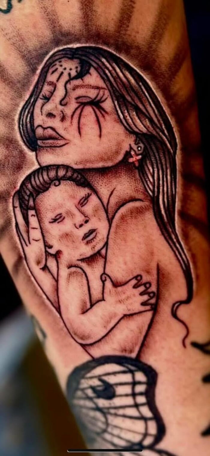 Tattoo of a woman holding a baby with distorted features as a permanent inked mistake on skin.