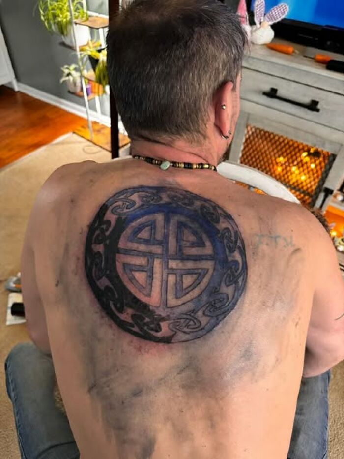 Man showing a large tattoo on his upper back with faded and smudged ink, showcasing a permanent mistake in inked design.
