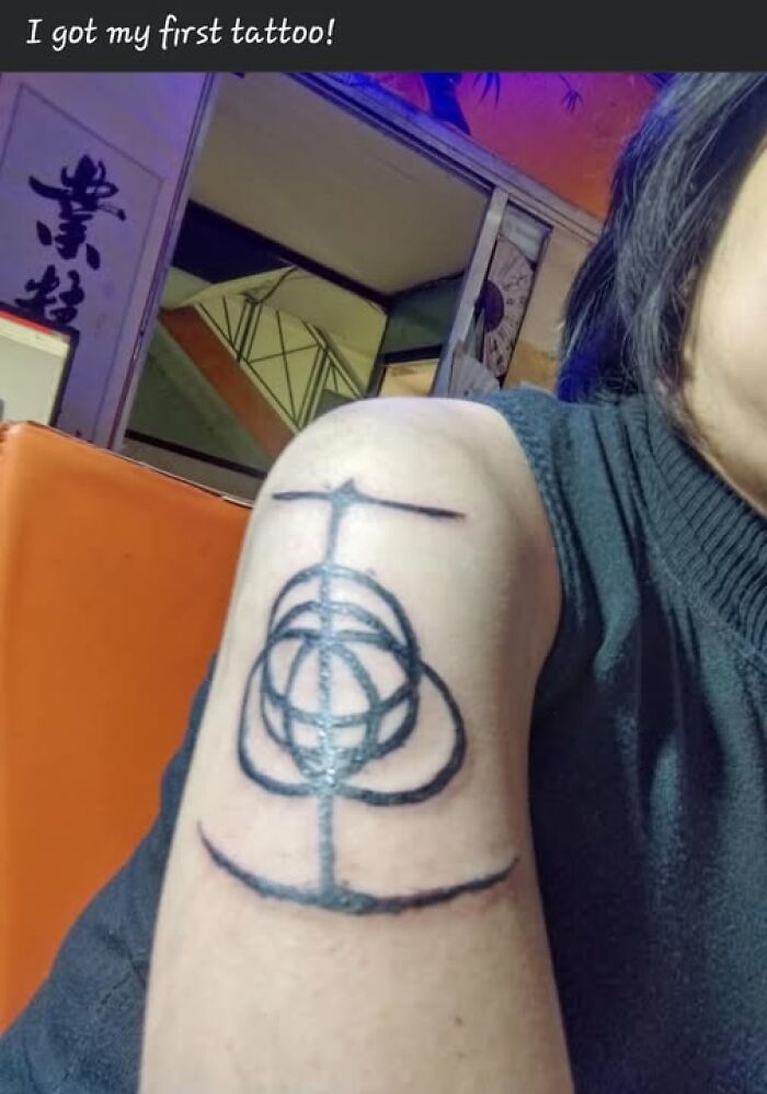 Person showing a tattoo on their upper arm with a design that looks like a permanent mistake in ink.