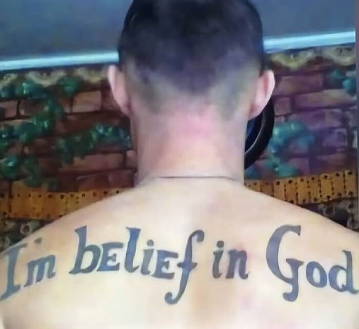 Tattoo with a permanent mistake reading Im belief in God on a man's upper back, showing inked errors meant to look cool.
