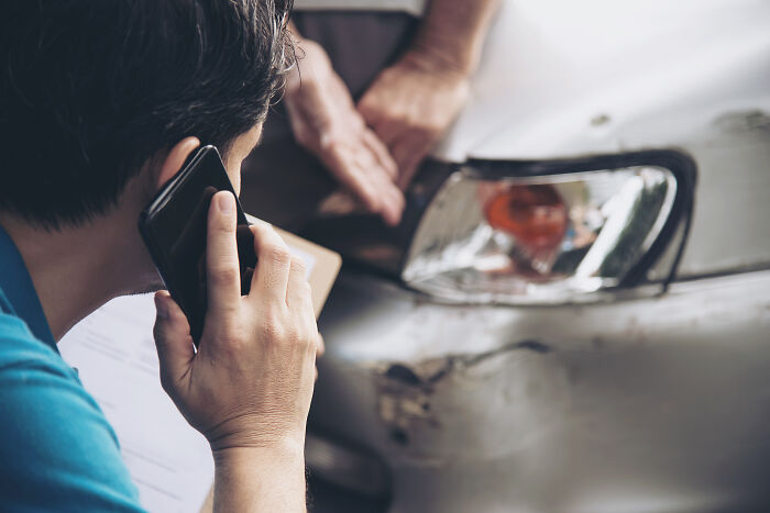 Person on phone inspecting a car's damaged front while discussing quick money and weird ways to earn.