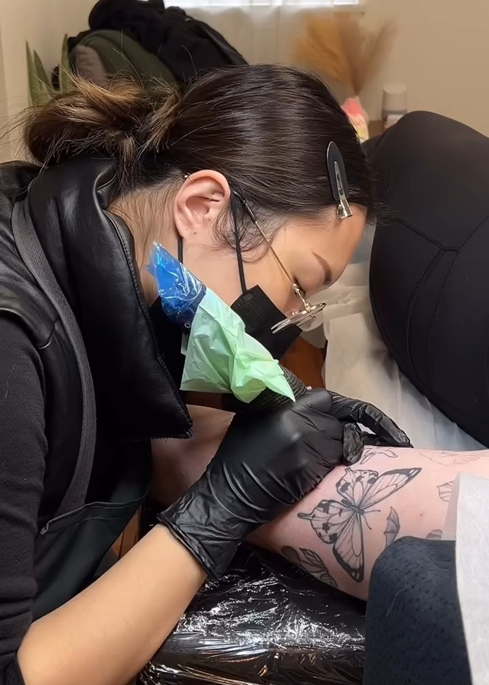 Tattoo artist wearing gloves and mask creating a detailed butterfly tattoo on a client's arm during the tattoo boom.
