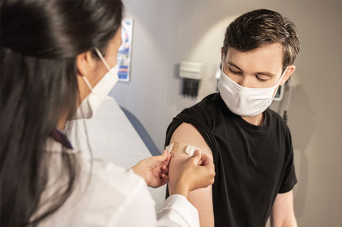 Healthcare worker applying a bandage to a young man’s arm after vaccination, highlighting future innovations changing humanity.