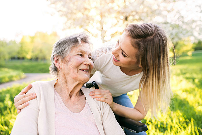 Young woman smiling at elderly woman in wheelchair outdoors, representing changes coming to humanity in next 10 to 15 years.