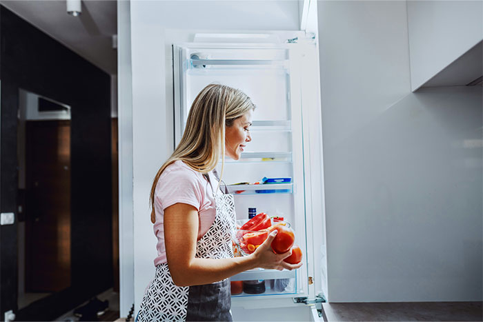 Woman holding tomatoes while standing in a kitchen in front of an open fridge, representing future innovations changing humanity.