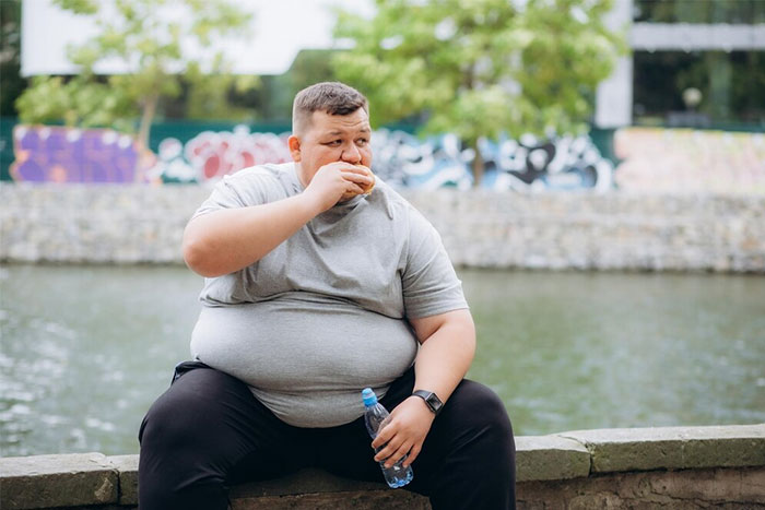 Man sitting by a river eating a sandwich holding a water bottle, illustrating future health changes impacting humanity soon.