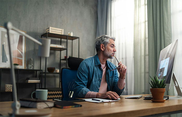 Middle-aged man at desk, thoughtfully looking at computer screen, considering future innovations that will change humanity.