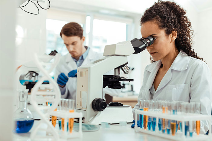 Female scientist using a microscope with test tubes in lab, focusing on innovation changing humanity in the next 10 to 15 years