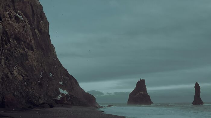 Rock formations rising from the ocean near a rugged coastline, showcasing one of the wonders that prove the world is still full of magic.