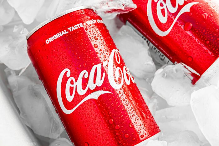 Red Coca-Cola cans chilled in ice with water droplets, illustrating food prices side-by-side comparisons from the 1980s and now.