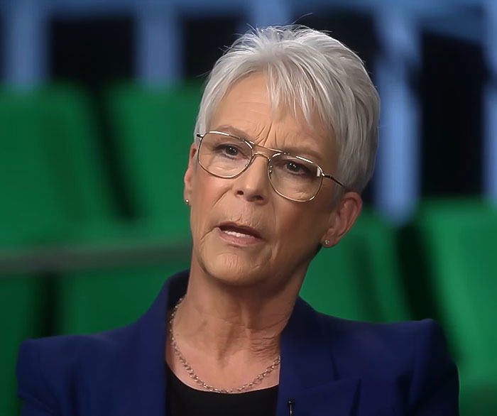 Jamie Lee Curtis with short white hair and glasses, discussing plastic surgery prompted by a cameraman remark. Jamie Lee Curtis with short white hair and glasses, discussing plastic surgery prompted by a cameraman remark.