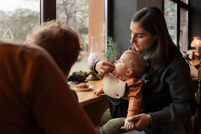 Traveling mom and dad sit by a window with their baby in a cozy restaurant, highlighting kindness from a Japanese waitress.