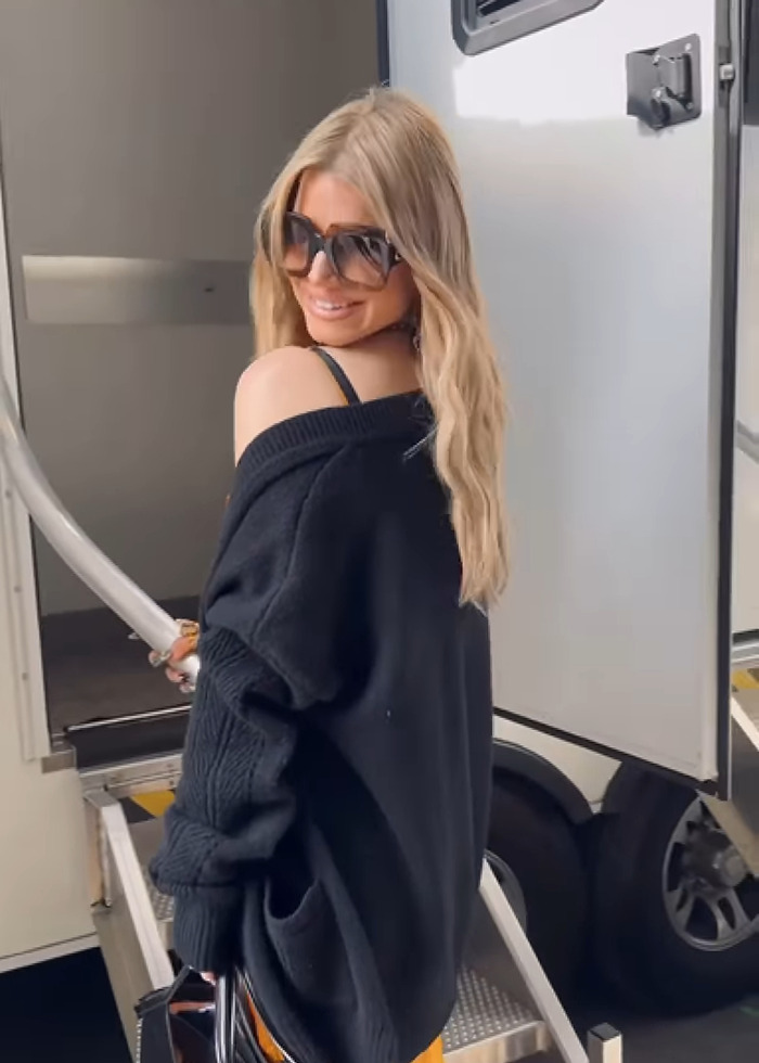 Jessica Simpson wearing sunglasses and a black sweater, smiling while boarding a trailer before live TV performance.