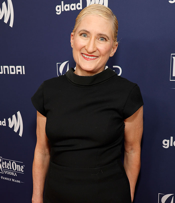 Singer Jill Sobule wearing a black dress at a GLAAD event, smiling against a dark blue branded backdrop. Singer Jill Sobule wearing a black dress at a GLAAD event, smiling against a dark blue branded backdrop.